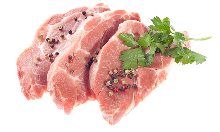 Three raw pork-chops side by side with parsely and peppercorns